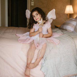 Young girl in a fairy costume sitting on a bed holding a flower.