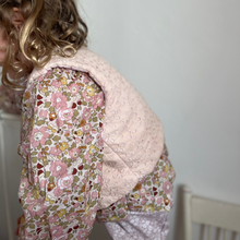 Load image into Gallery viewer, Child wearing a floral top with a beige vest against a white wall