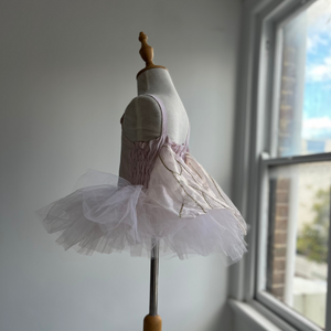 Mannequin with a white tutu dress on a wooden stand by a window