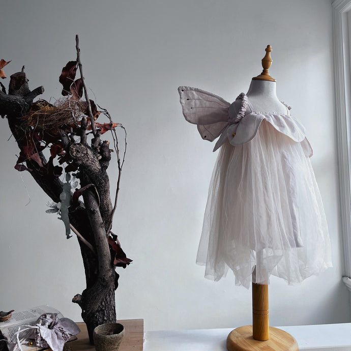 Mannequin with an off white dress on a wooden stand against a plain wall.