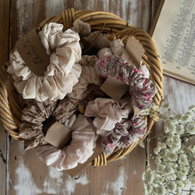 Load image into Gallery viewer, Basket of scrunchies on a wooden surface with a floral arrangement.