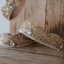 Load image into Gallery viewer, Gold glittery tiaras on a wooden surface with a blurred background