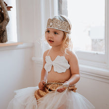 Load image into Gallery viewer, Young girl in a white and gold dress with a headband, sitting indoors.