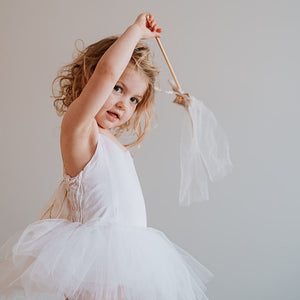 Young girl in a white dress holding a decorative ribbon against a plain background