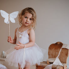 Load image into Gallery viewer, Young girl in a white dress holding a butterfly wand in a room with wooden furniture.