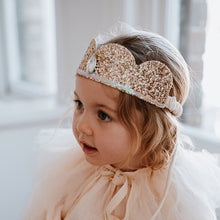 Load image into Gallery viewer, Young child wearing a sparkling tiara and white dress in a softly lit room.